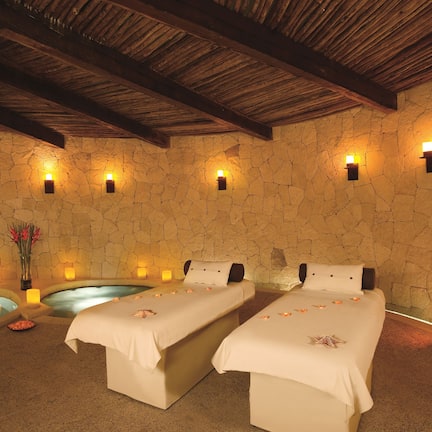 A spa room with two beds, a stone wall, wooden beams, and two hot tubs.