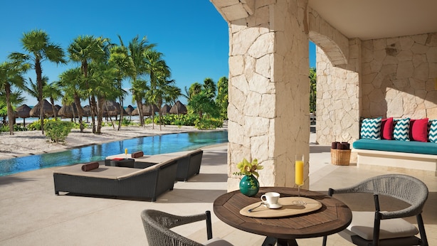 A poolside area with lounge chairs, a table with a vase and a glass, and a stone wall. - Secrets Maroma Beach Riviera Cancun - Adults Only - All inclusive (Playa del Carmen)