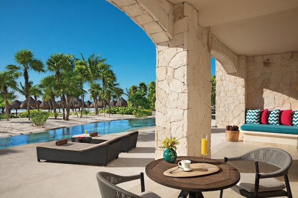 A poolside area with lounge chairs, a table with a vase and a glass, and a stone wall. - Secrets Maroma Beach Riviera Cancun - Adults Only - All inclusive (Playa del Carmen)