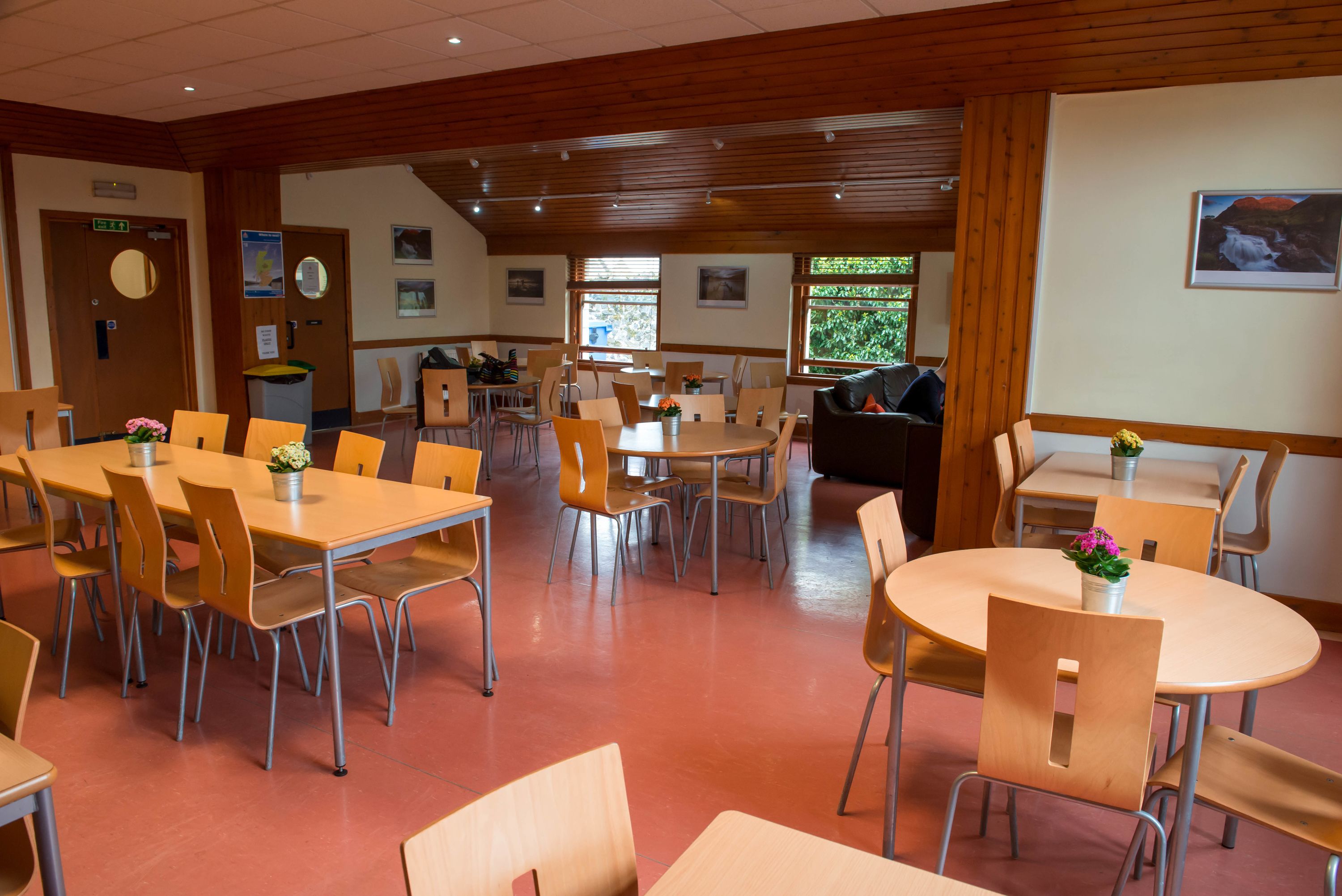 A dining area with multiple tables and chairs, wooden walls, and a view of the outdoors through large windows.
