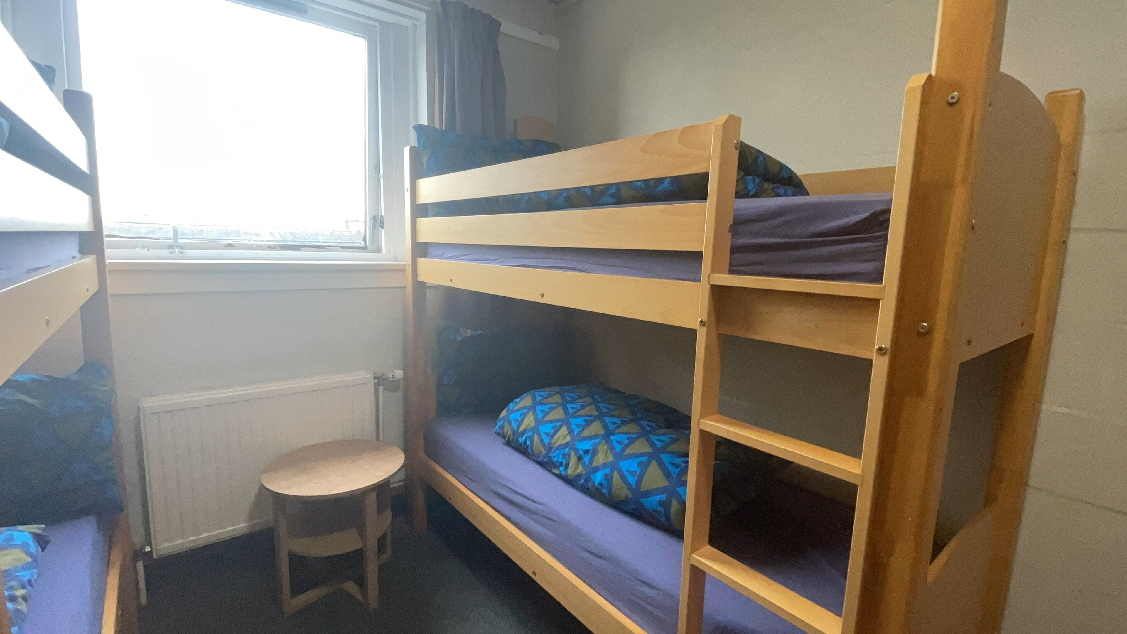 A bunk bed room with a small stool and a window.