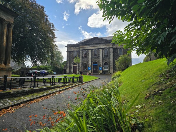 A building with classical architecture, a paved pathway, and a grassy area with plants. - Stirling Youth Hostel (Stirling)