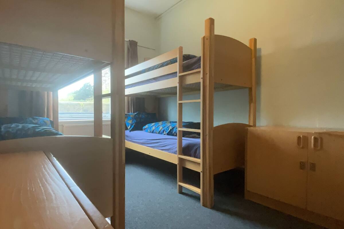 A bunk bed room with a window, a desk, and a wardrobe.