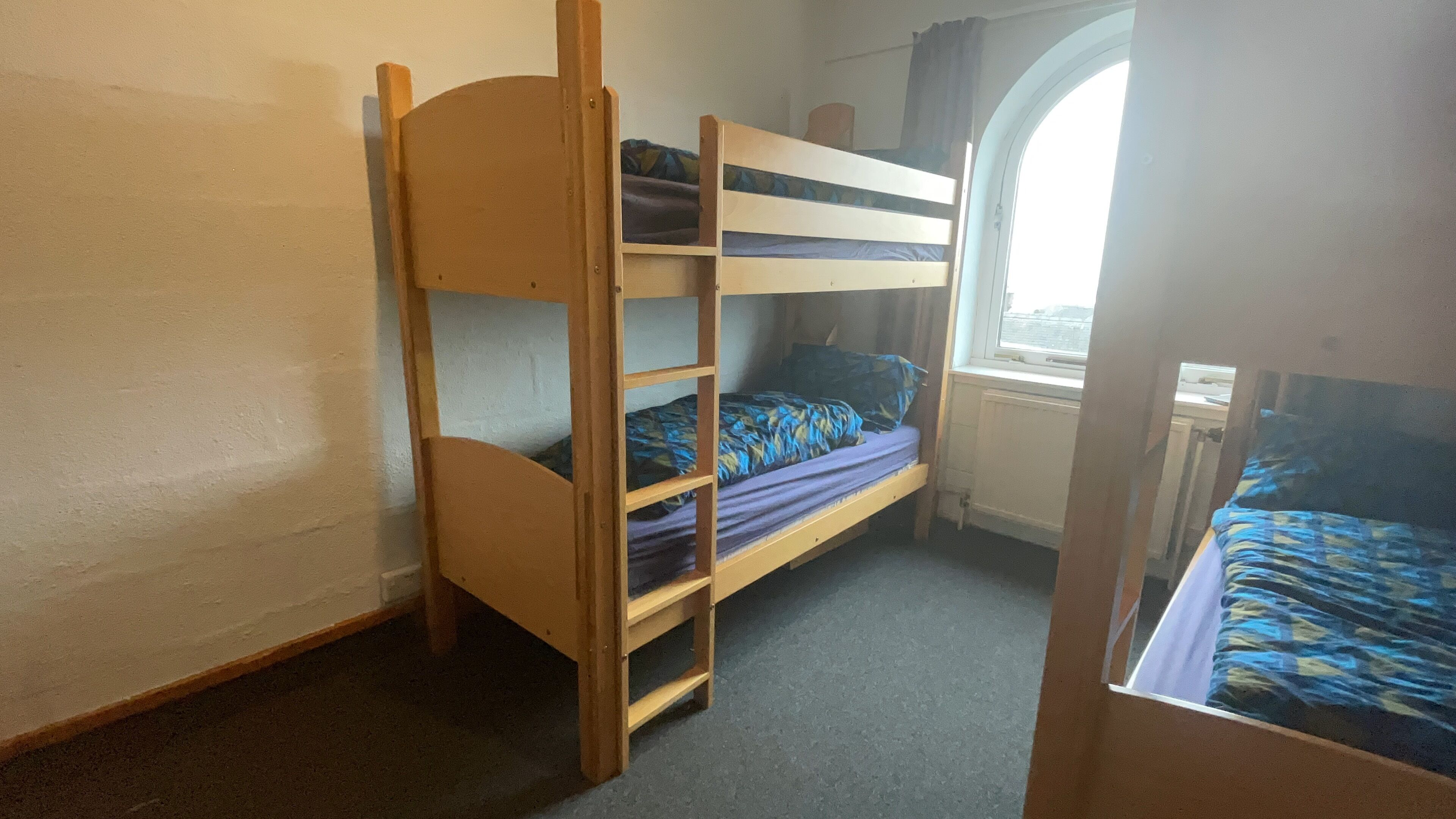 A bunk bed room with a window, a radiator, and a door.