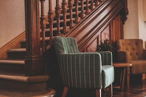 Una escalera con balaustres de madera, un sillón tapizado de verde y un banco de madera.