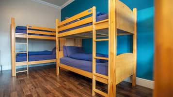 A room with three bunk beds, wooden flooring, and teal walls.