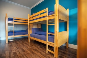 Una habitación con tres literas, suelo de madera y paredes color aguamarina.