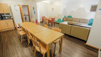 Un comedor con mesa y sillas de madera, una kitchenette, un sofá y una pared con un diseño de montaña.