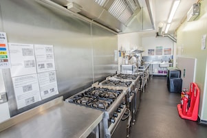 Una cocina industrial con electrodomésticos de acero inoxidable, un extintor de incendios y señalización instructiva en las paredes.