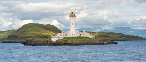 A lighthouse on a small island with a rocky shoreline and a mountainous backdrop.