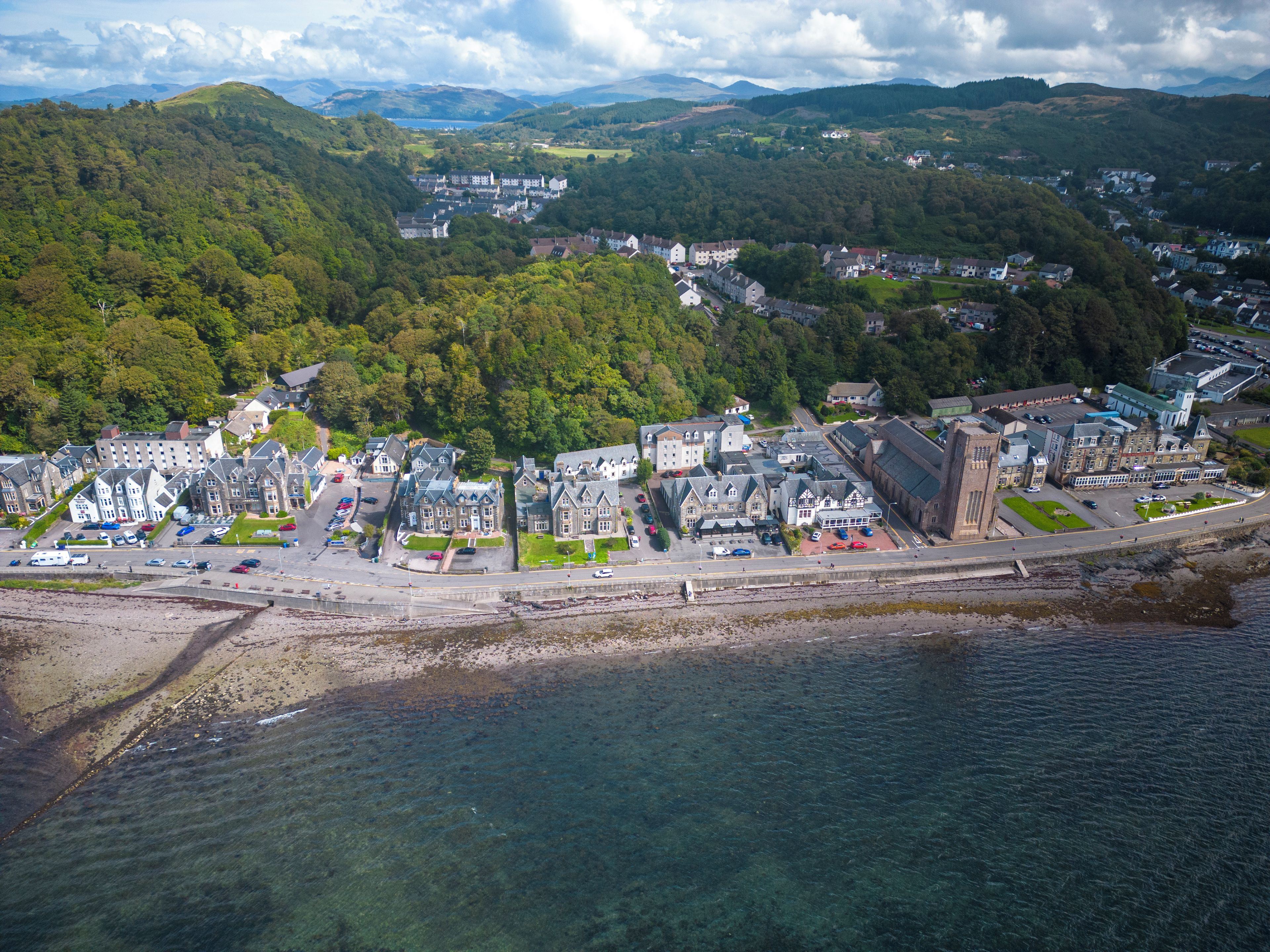 An aerial view of a coastal town with a mix of residential and commercial buildings, a prominent church, and a clear view of the coastline.