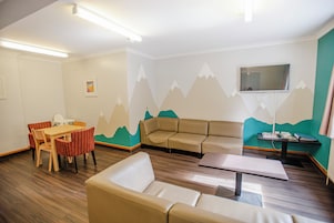 Una habitación con suelo de madera, un sofá, una mesa, un televisor montado en la pared y un cuadro de montañas.