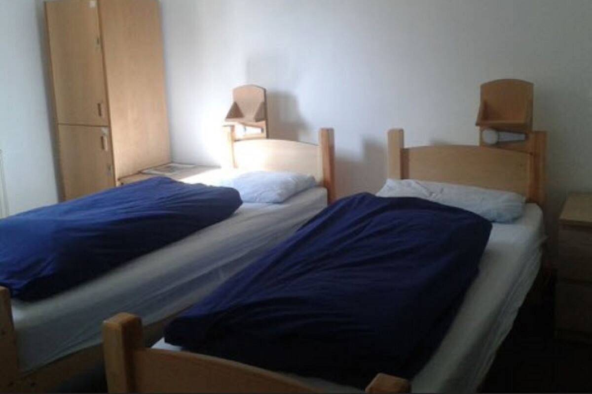 A simple room with two wooden beds, a wooden wardrobe, and a small table.