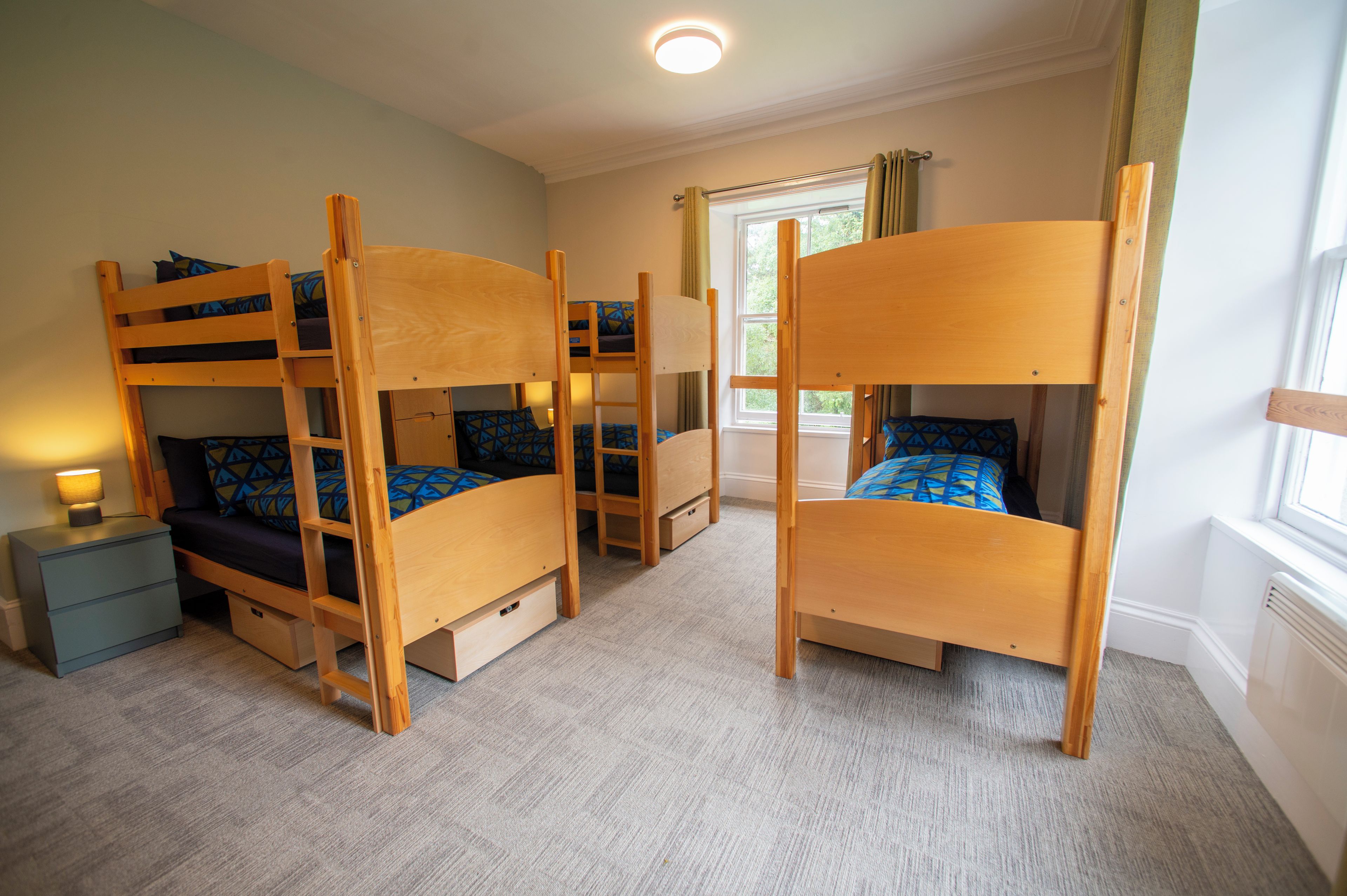 Quarto com beliches, mesa de cabeceira e janela com cortinas.