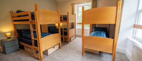 Quarto com beliches, mesa de cabeceira e janela com cortinas.