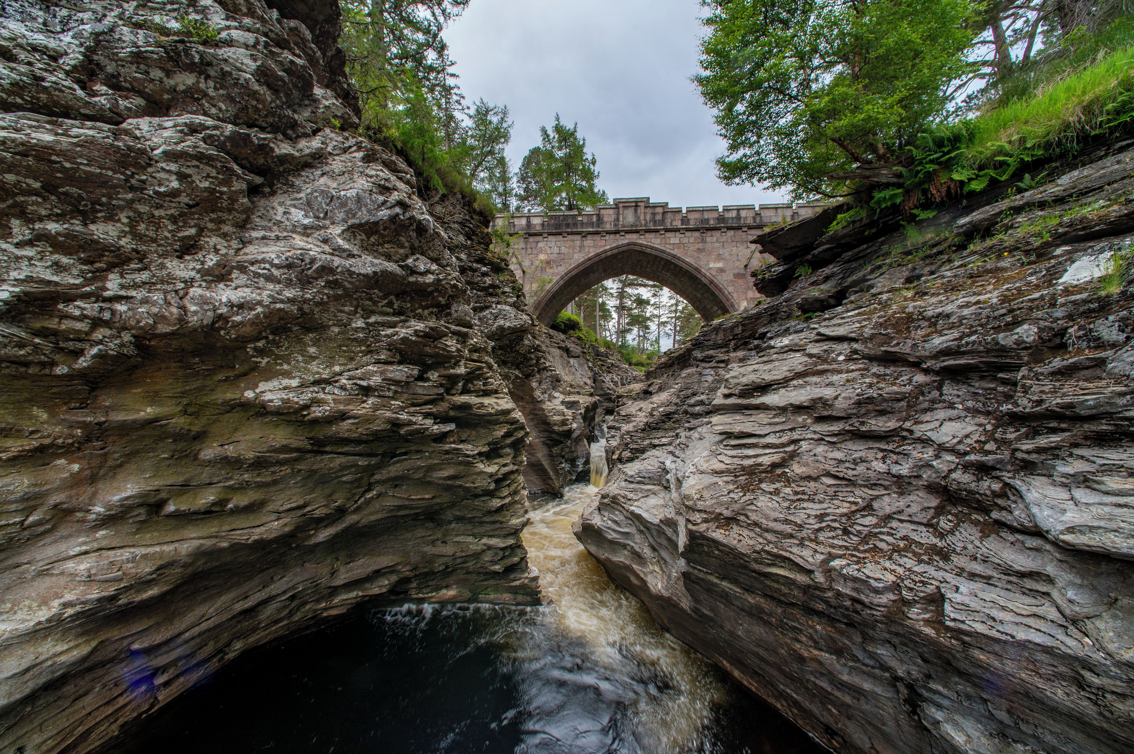 A stone bridge arching over a rocky gorge with a flowing stream below.