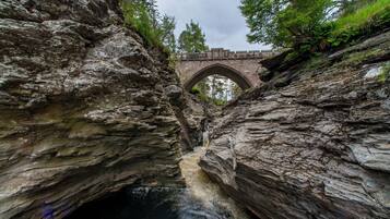 A stone bridge arching over a rocky gorge with a flowing stream below.