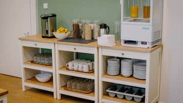 A buffet setup with various food containers, a coffee machine, and stacked plates and cups.