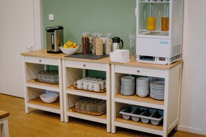 A buffet setup with various food containers, a coffee machine, and stacked plates and cups. - Braemar Youth Hostel (Ballater)