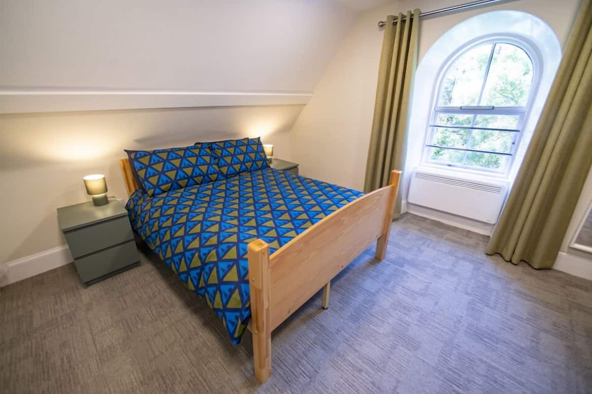 A bedroom with a bed, a nightstand, a lamp, and a window with curtains.