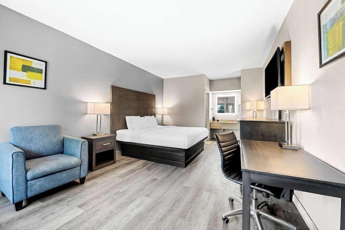 Ein modernes Hotelzimmer mit Bett, Schreibtisch, Stuhl, Sofa und Fernseher.