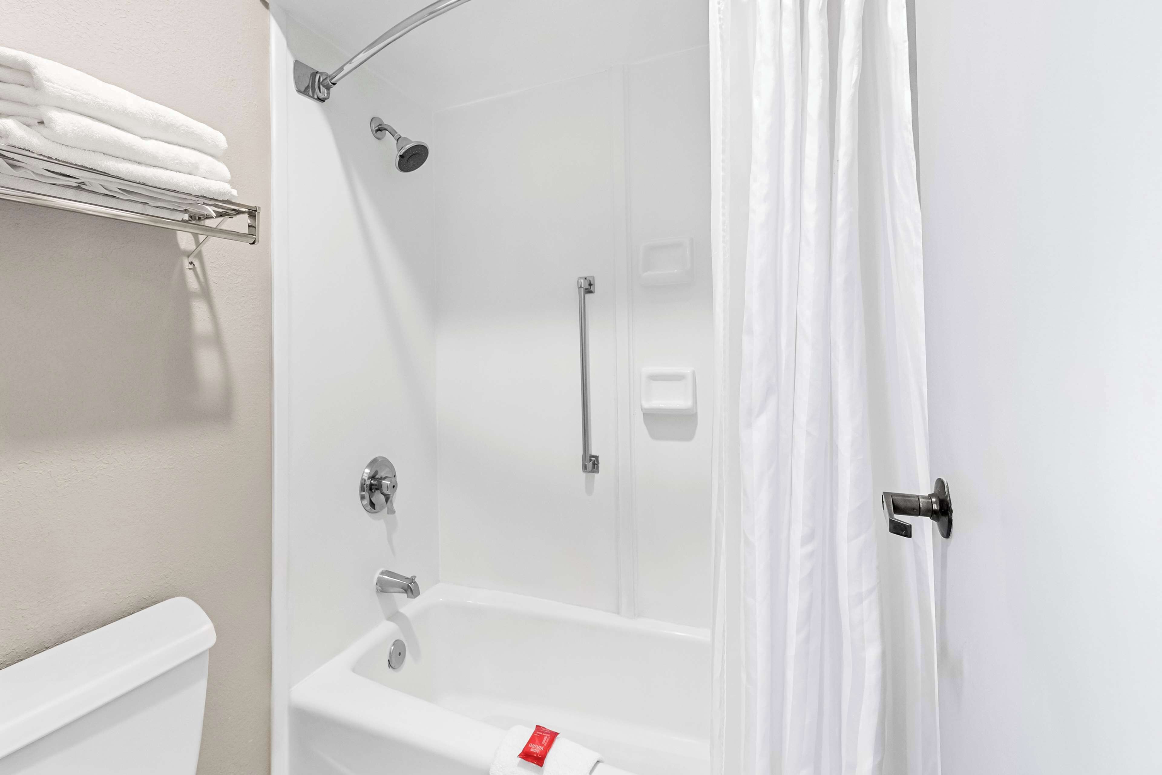 A bathroom with a white bathtub, a shower, and a toilet. There is a towel rack with folded towels.