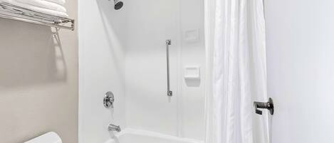 A bathroom with a white bathtub, a shower, and a toilet. There is a towel rack with folded towels.