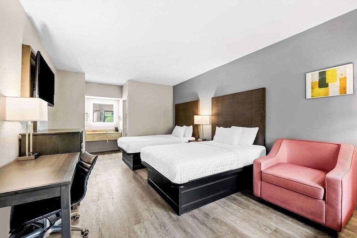 Ein Hotelzimmer mit Schreibtisch, zwei Betten, einem roten Sessel und einem großen Fenster.