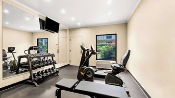 A gym with exercise equipment, a bench, and a TV mounted on the wall.