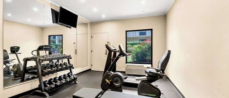 Een sportschool met trainingsapparatuur, een bank en een aan de muur bevestigde televisie.
