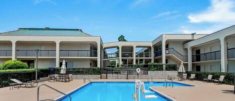 A hotel with a swimming pool, outdoor seating, and a clear blue sky.