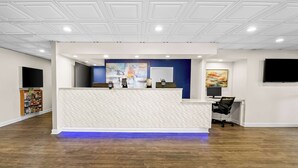 Een receptiegedeelte met een wit receptiebalie, een blauwe accentmuur en een bevestigde televisie.