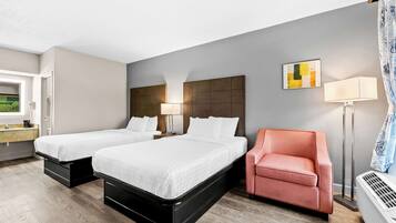 A modern hotel room with two beds, a sofa, a desk, and a window with a view.