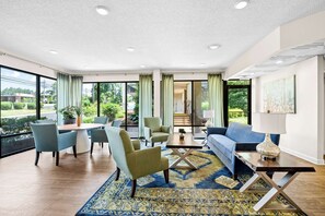 A spacious living room with a dining area, large windows, and a view of greenery outside.