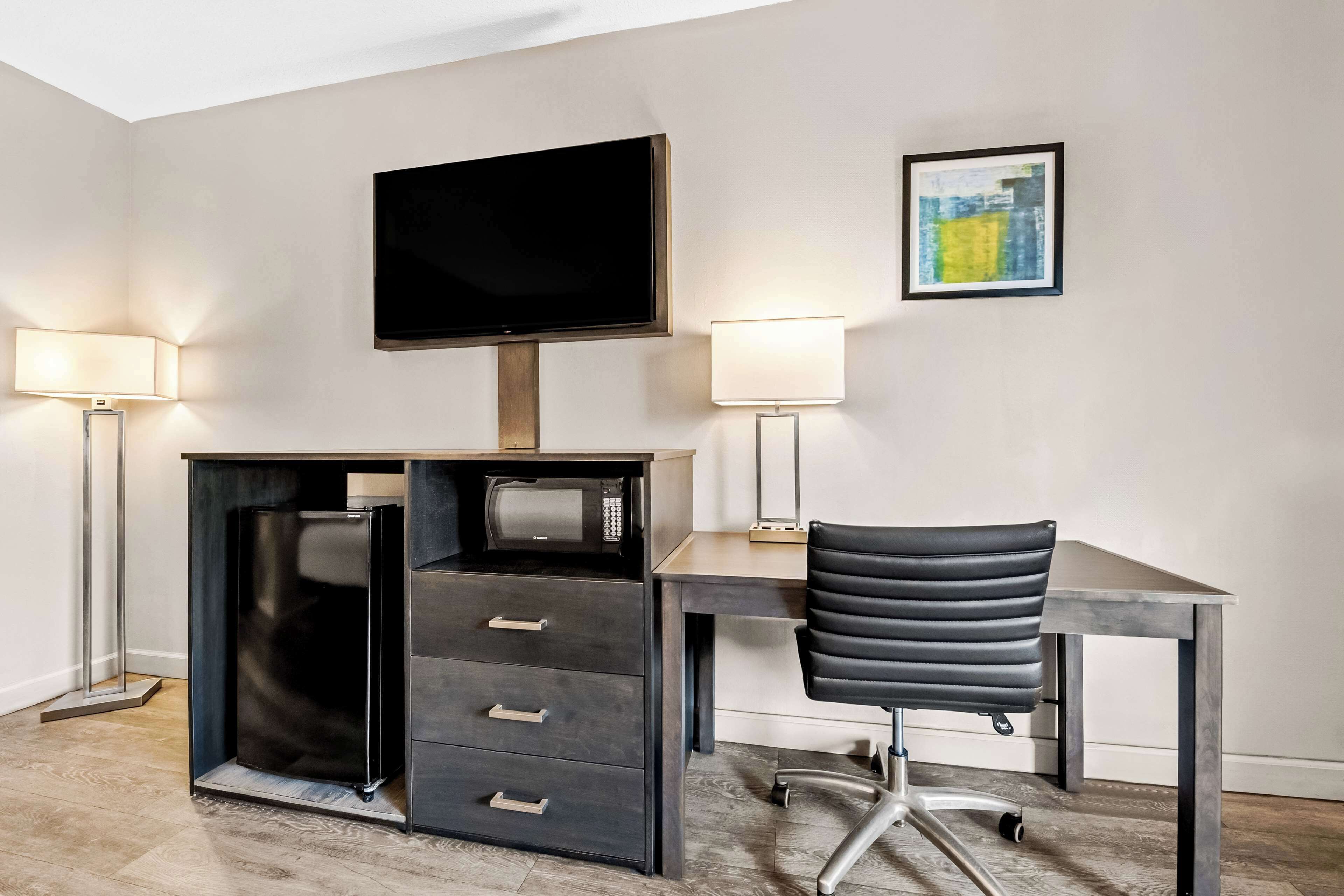 Un espacio de oficina moderno con un escritorio, una silla, un televisor de pantalla plana y dos lámparas fijadas a la pared.