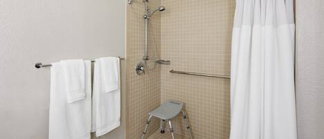 A small, tiled shower area with a grab bar, a step stool, and a white shower curtain.