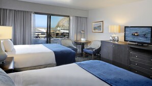 A hotel room with two beds, a desk, a chair, a television, and a view of a mountain and a body of water. - Blue Sail Inn (Morro Bay)
