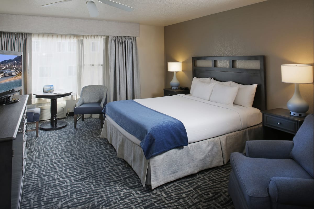 Quarto de hotel com uma cama grande, uma escrivaninha com cadeira, uma mesinha e vista para o exterior.