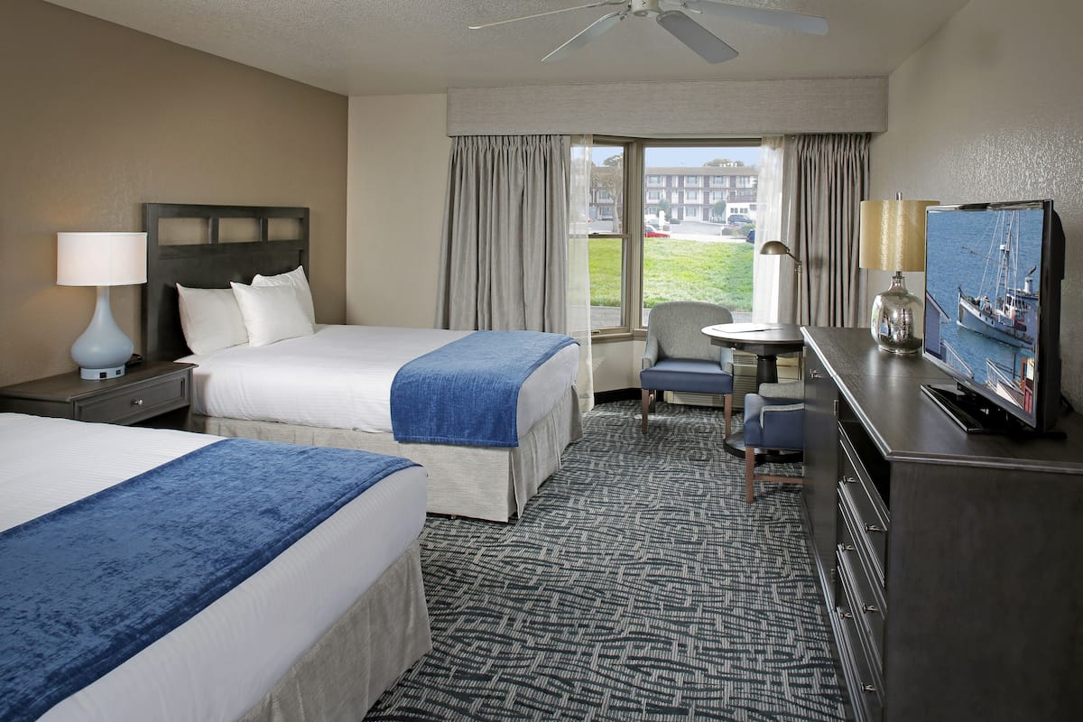 Quarto de hotel com duas camas, uma escrivaninha, televisão e vista para o exterior.