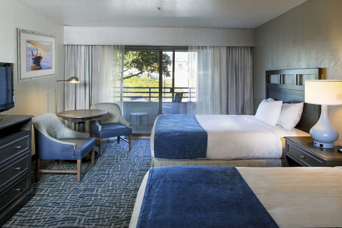 Quarto de hotel com cama, escrivaninha, cadeira, televisão e janela com cortinas.