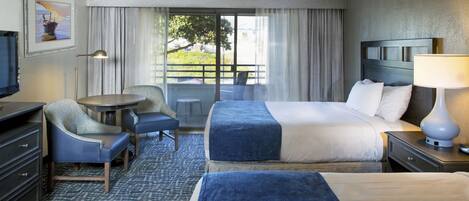 A hotel room with a bed, a desk, a chair, a TV, and a window with curtains.