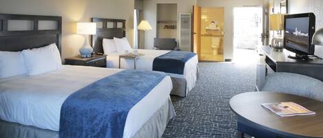 A hotel room with two beds, a desk with a computer, a TV, and a seating area with a magazine.