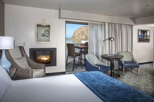 Una habitación de hotel con una cama, dos sillones, una mesita, una chimenea y vista al mar.