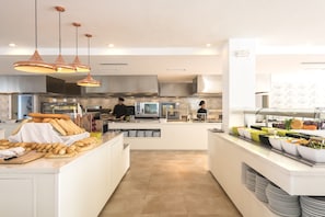 A modern kitchen with a central island, overhead lighting, and a buffet area with various food items. - Palm Garden Apartments (Alcúdia)