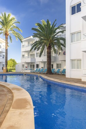 Una piscina al aire libre, sombrillas, sillones reclinables de piscina