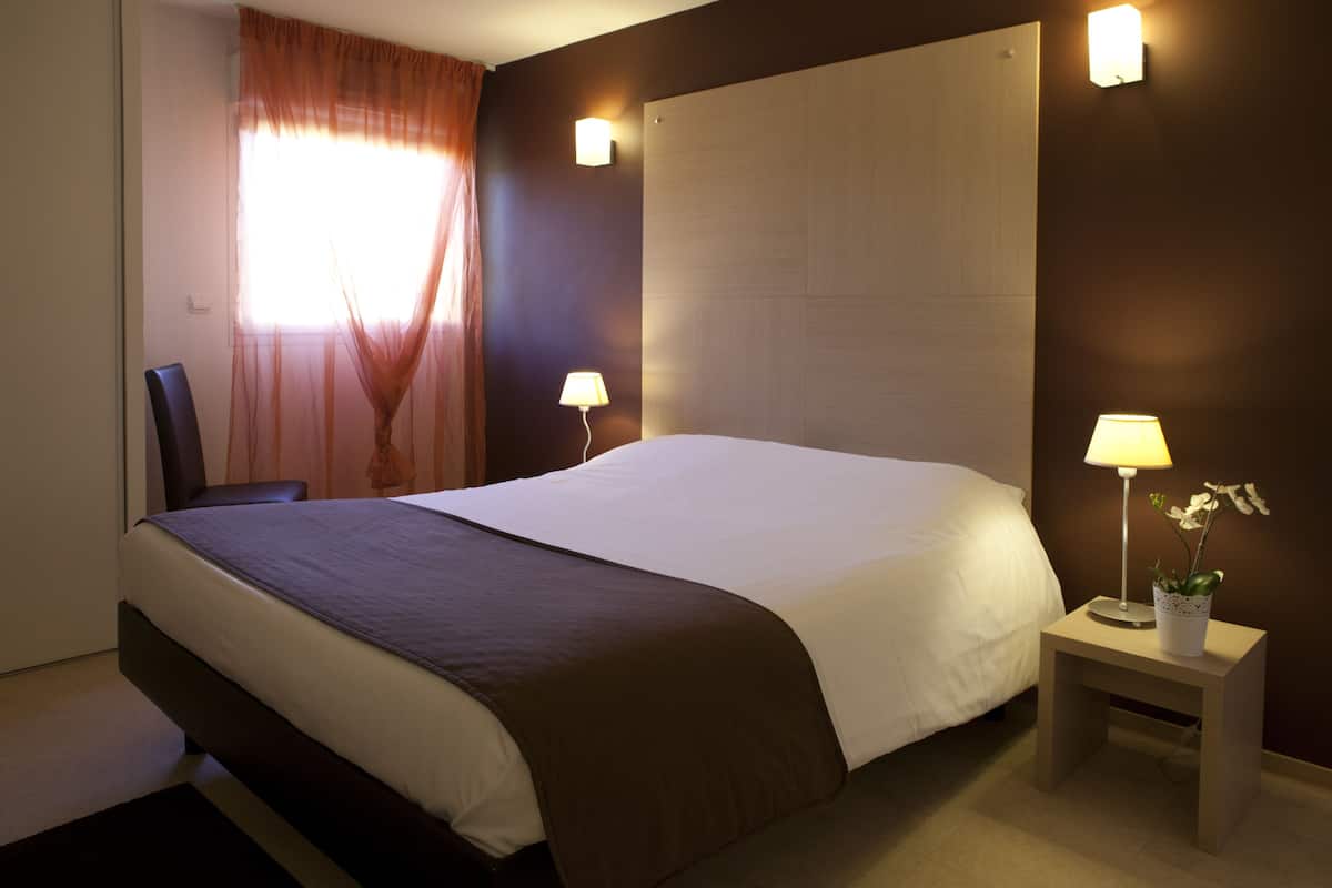 A hotel room with a large bed, two bedside lamps, a chair, and a small table with a plant.
