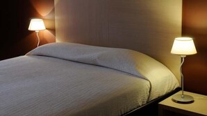 Una cama bien hecha con una colcha blanca y dos lámparas de noche sobre una mesita de madera.