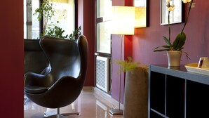 Un interior moderno con un sillón de cuero negro, una planta en maceta y un jarrón con flores sobre una consola.