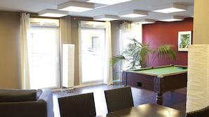 Una sala de billar con mesa de pool, dos sillas, un sofá y una planta en maceta.