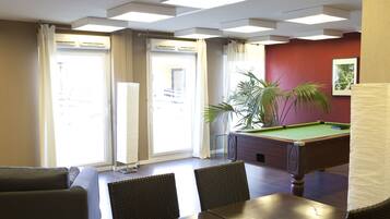 A billiards room with a pool table, two chairs, a sofa, and a potted plant.